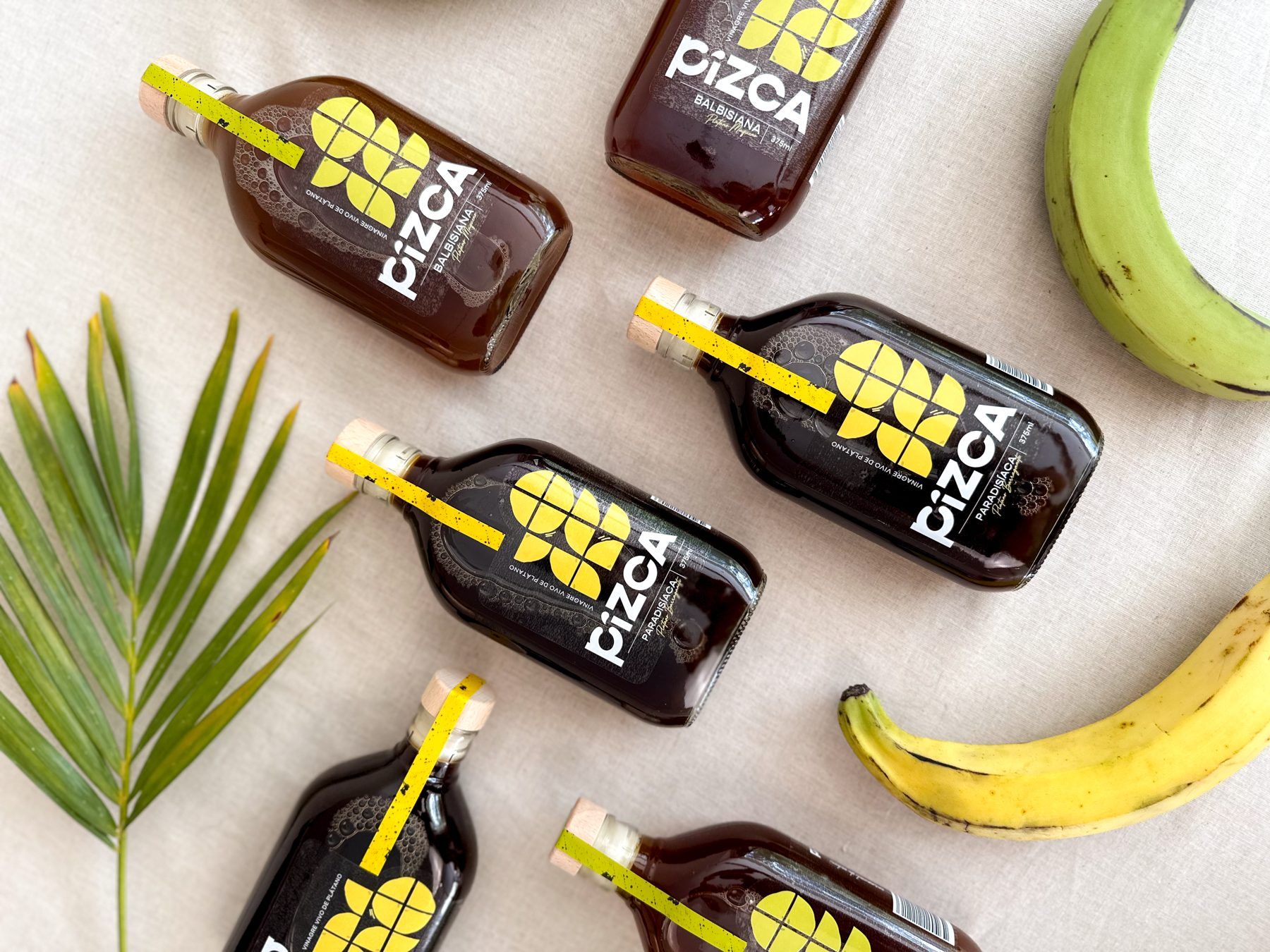 Pizca bottles among green and ripe plantains and palm leaves