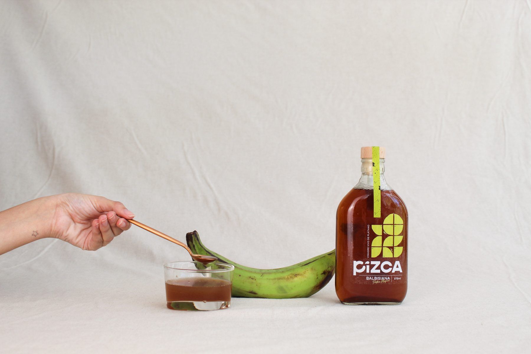 A spoon pouring vinegar next to a green plantain